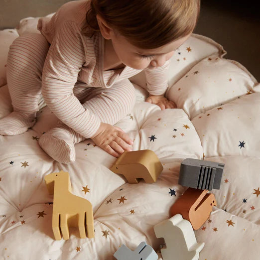 Kleinkind im gestreiften Pyjama spielt auf einem gepolsterten Spielteppich mit Holzspielzeug in Tierform.