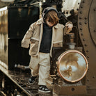 Kind in beiger Donsje-Kleidung balanciert auf einer alten Lokomotive – Black Friday Kinder-Mode mit bis zu 25 % Rabatt bei LibertyKids